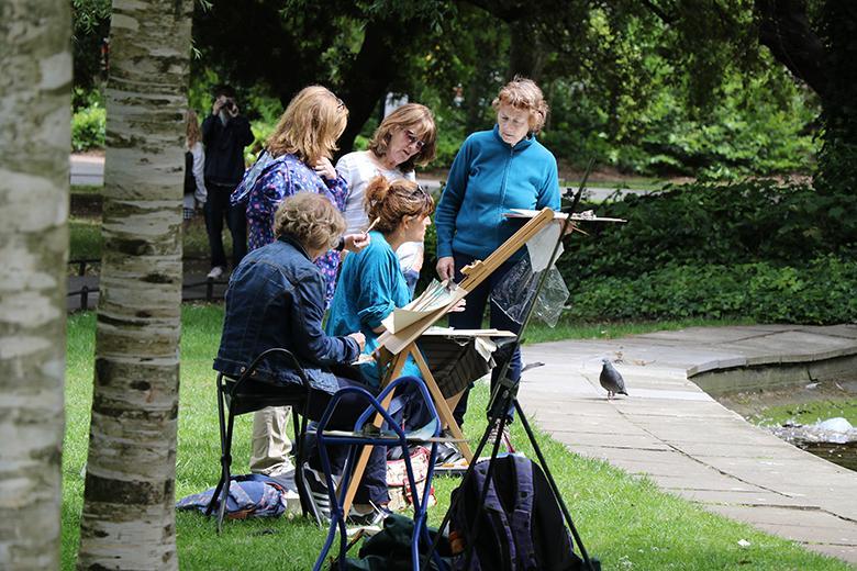 Photo of a group of five women painting at at easel outdoors.