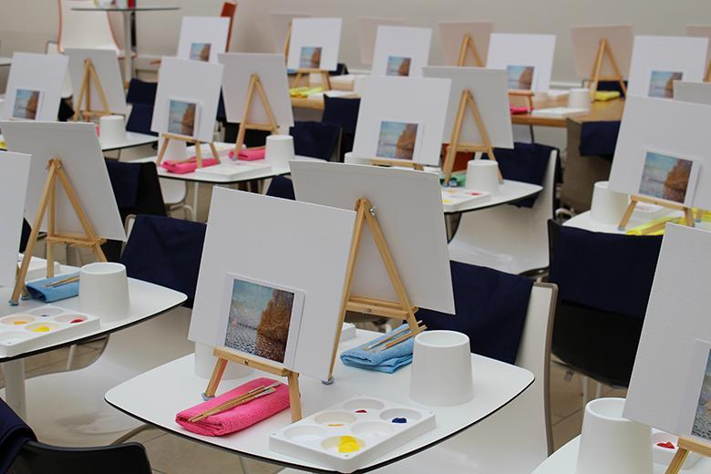 Photo of a room set up for an art class with lots of easels and canvases on tables