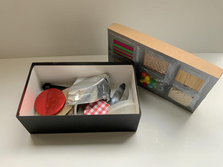 A shoe box filled with household objects, with textured materials taped to the lid