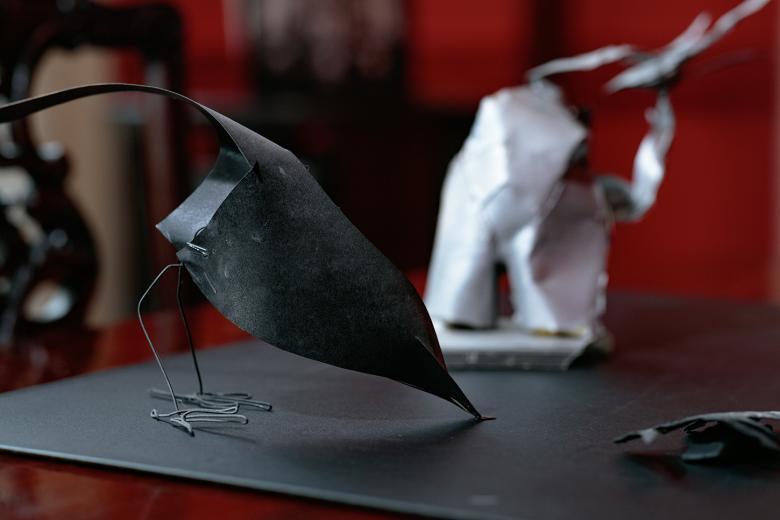 A dark grey maquette of a bird stands on a table, with a red wall visible behind