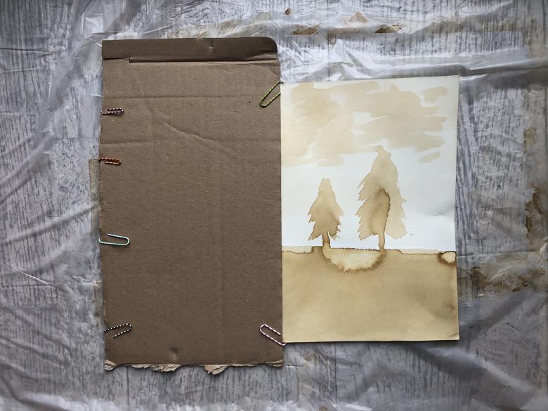 Brown ink painting of trees next to a sheet of cardboards with paperclips attached to it. 