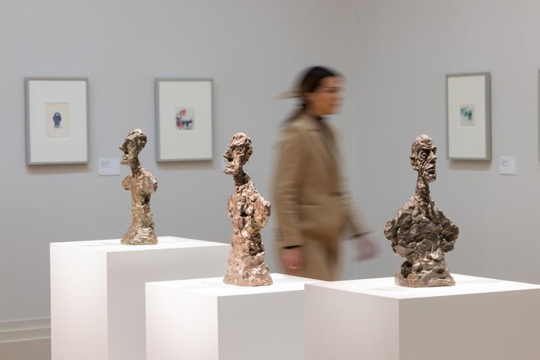 Woman walking past three sculptures in the exhibition Giacometti: From Life