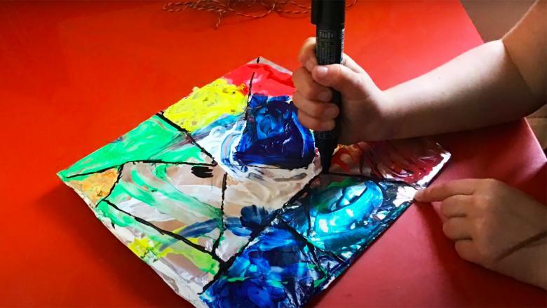 Young child making a stained glass inspired painting with colourful paint