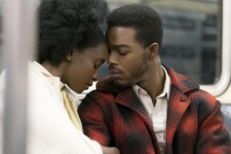 A close-up of two people sitting together in a subway carriage. They are turned towards each other, and the woman rests her forehead on the man's.