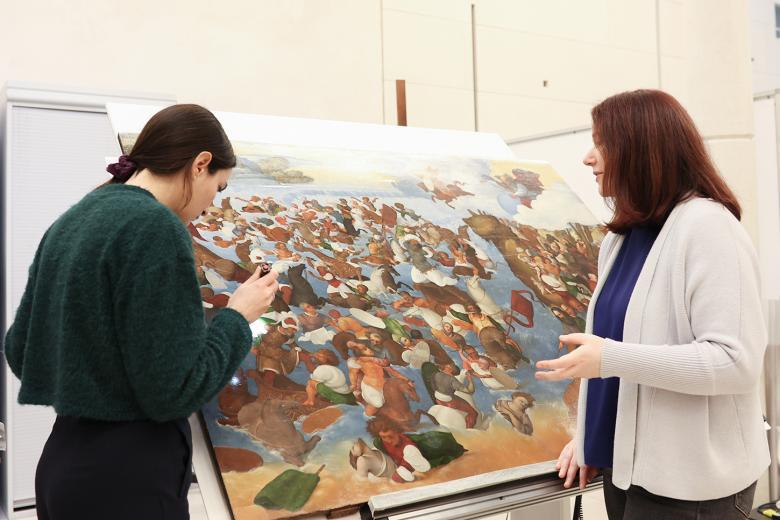 Two women look closely at a painting in a conservation studio