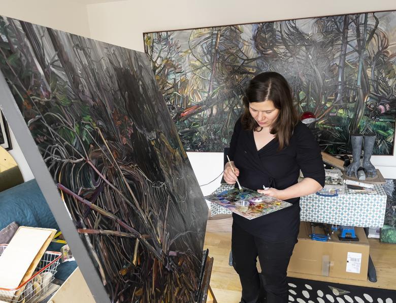 Photo of Vera Klute painting at an easel in her studio