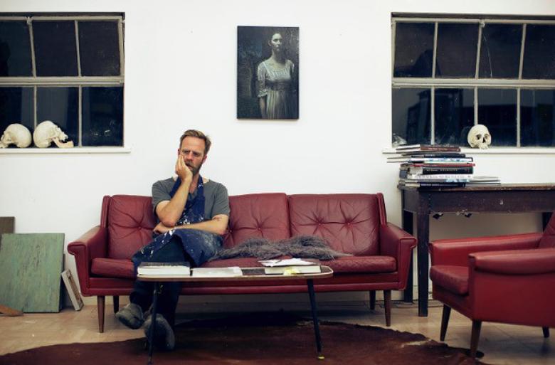 Photo of Stuart Pearson Wright sitting on a red leather couch in his studio