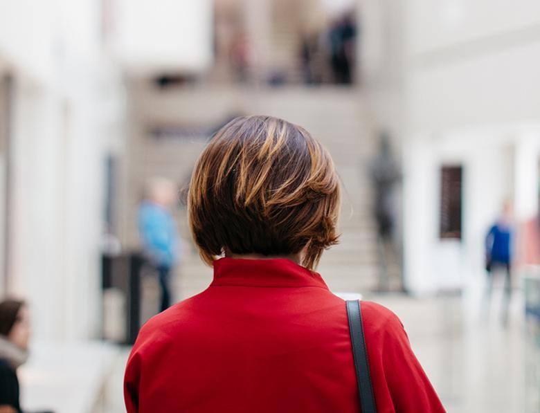 A woman with her back to the camera, wearing a red coat, standing in the National Gallery of Ireland.