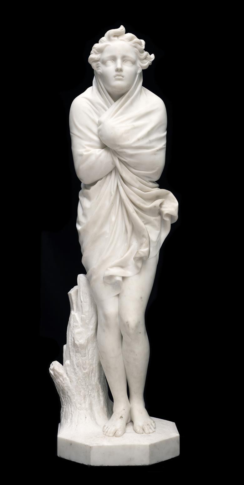 A marble sculpture of a female figure, wrapping a shawl tightly around herself against the cold