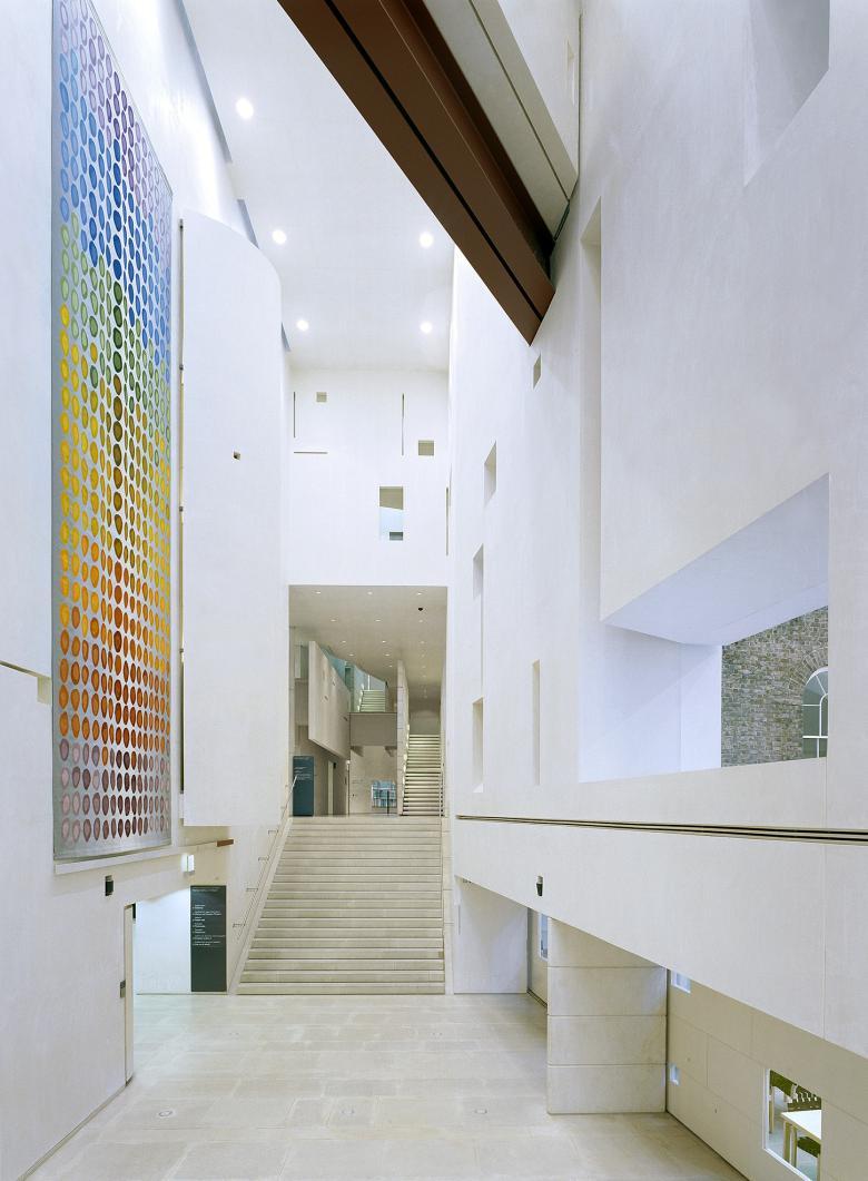 A view of the Gallery's Millennium Wing. The walls are white, and the ceiling is high. To the left, there is a large, colourful tapestry hanging on the wall.