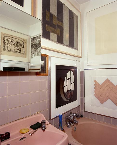 Photo of the corner of Alexander Walker's bathroom with pink sanitary ware and tiles, with framed artworks covering the walls.