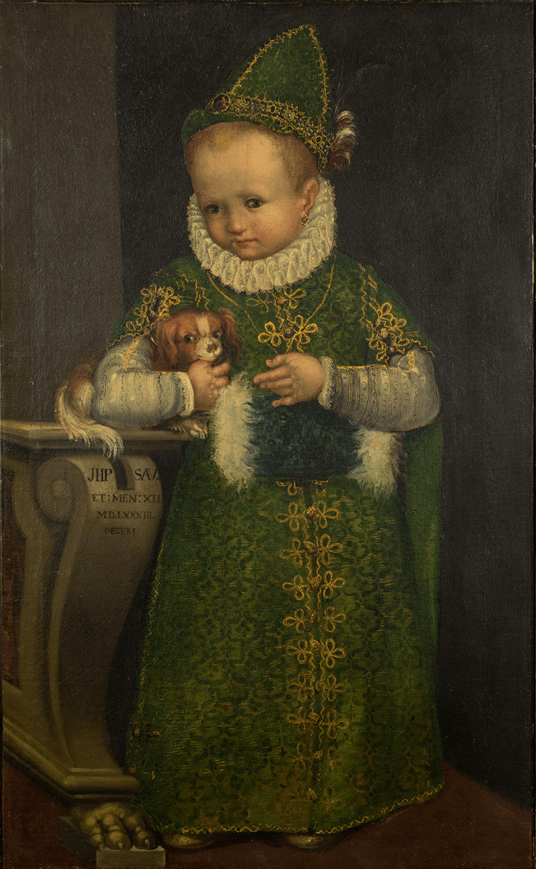 Portrait of a small child in a green dress with white ruff and a green pointed hat, holding a small dog.