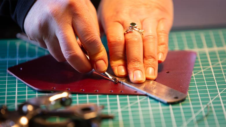 Close up image of hands scoring a piece of leather with a small tool