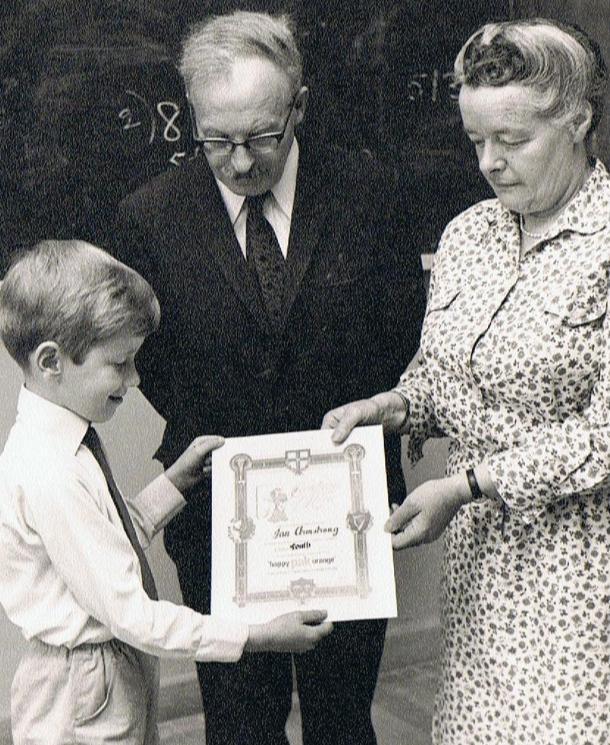 A black and white photograph of a man and and woman giving a young child a prize