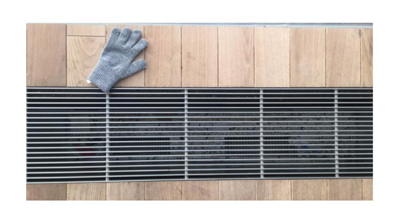 Photo of a blue woolen glove lying on a wooden floor beside a metal vent.