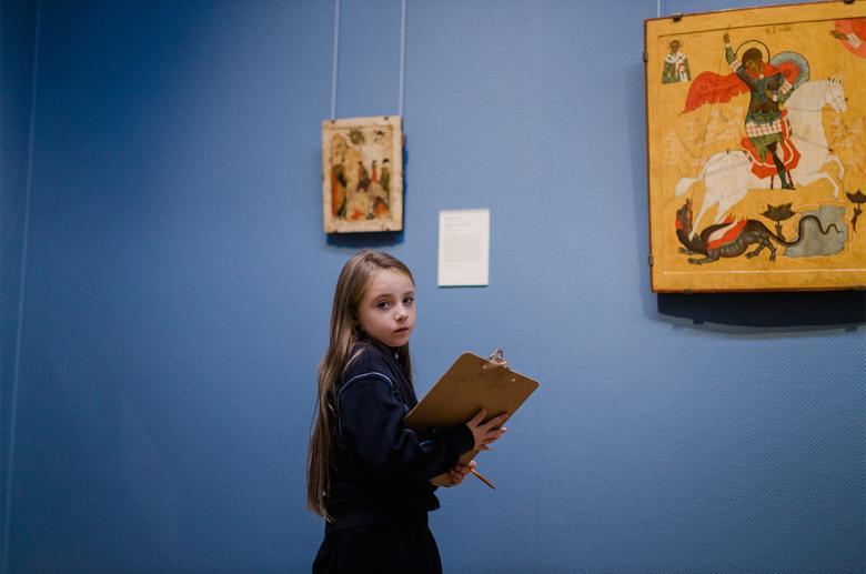 A young child stands in front of a painting with a clipboard.