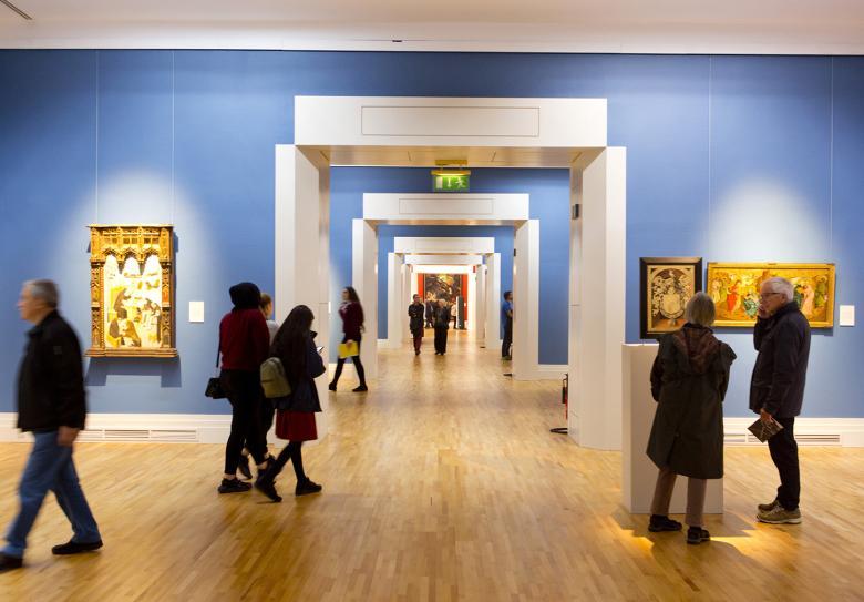 View of people in an art gallery with blue walls and gilt-framed paintings