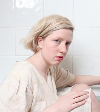 Still image from a video showing a young woman wearing white and seated in a bath full of water.