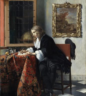 Detail of a man writing at a desk covered in a heavily patterned cloth.