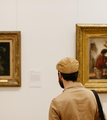 A man standing in front of two gilt-framed paintings in a gallery