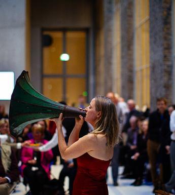 Photo of people attending an event with a woman playing speaking through a gramophone horn.