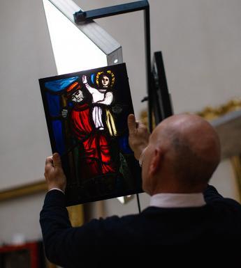 Photo of a man with his back to the camera, holding up a piece of stained glass so that the light shines through it.