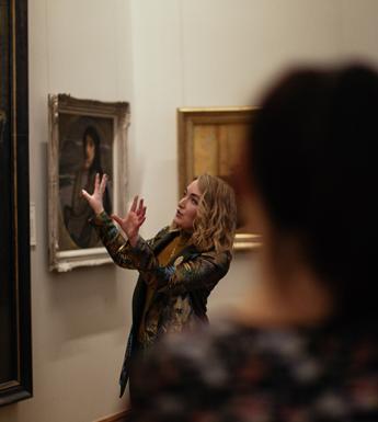 Photo of a tour guide speaking to a group of visitors in front of John Lavery's painting The Artist's Studio, in the National Gallery of Ireland.