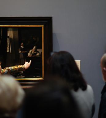 Photo of a tour guide speaking to a group of visitors in front of Vermeer's painting of a woman writing a letter in the National Gallery of Ireland.