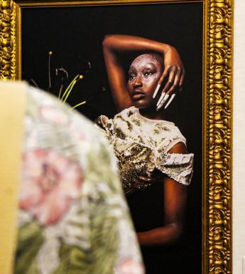 Photo, taken over a person's shoulder, of a gilt-framed photograph of a model.