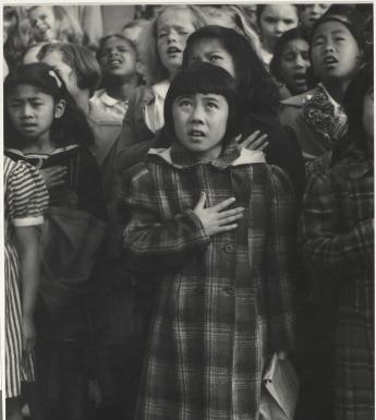 Black and white photo of children standing with one hand on their chests, pledging allegiance.