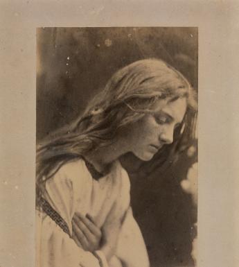 Black and white vintage photograph of a long-haired women with head bowed and hands crossed across chest