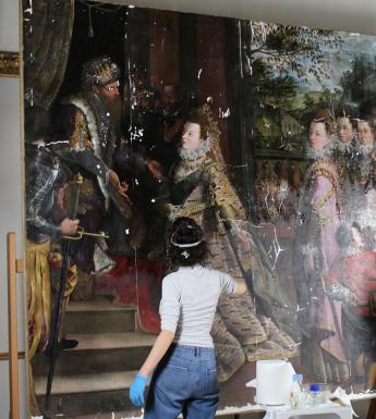 Two conservators applying isolating layer of varnish to a large oil painting