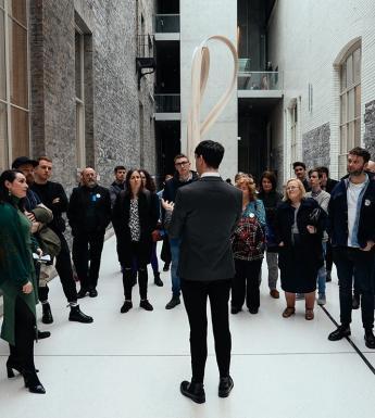 A group of people in a gallery gathered around a tour guide