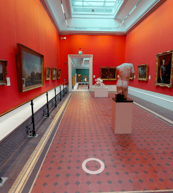 A view of a vibrant red gallery lined with paintings. On the tiled floor stand some sculptures