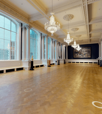 A long Gallery with chandeliers, polished wooden floors, and large windows at one side.
