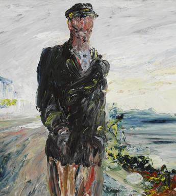 A man in a dark overcoat with his hands in his pockets, wearing a cap. In the background, the sea.  