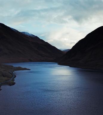A still from a documentary film, showing a lake surrounded by mountains