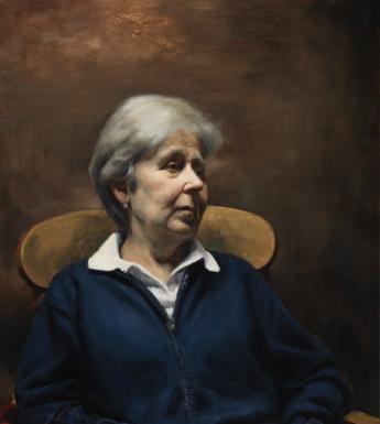 A woman sits in a chair, looking to the right of the frame. Her hands are in her lap.