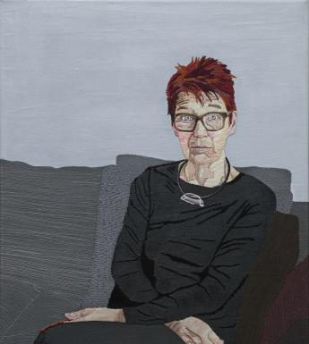 An embroidered portrait of a woman seated on a grey sofa, with her arms crossed in her lap.