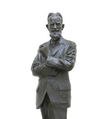 Bronze sculpture, 188cm high, of a bearded man wearing a suit, with arms crossed and left slightly raised