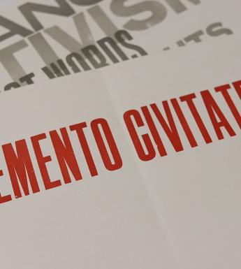 A sheet of paper with memento civitatem printed in red block capitals, with another sheet of paper visible beneath with fragments of words including activism and change