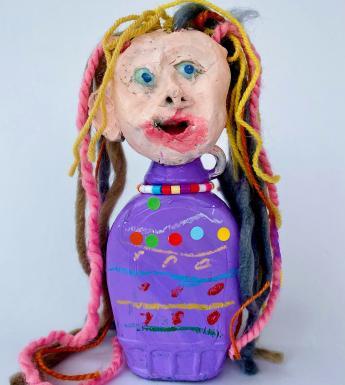 Sculpture of a female head with blue eyes and multi-coloured hair on a purple stand with coloured beads