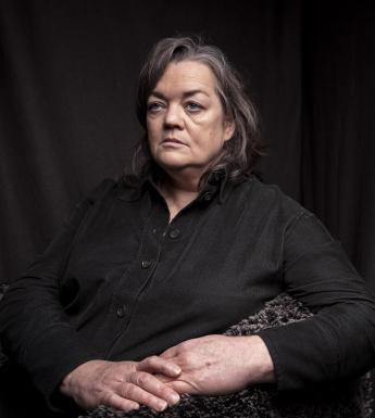 Photograph of a female figure with short grey hair and a black top on a black background