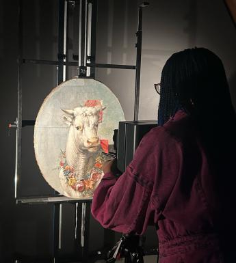A small oval painting of a bull stands on an easel; someone stands in front of it taking an infrared reading