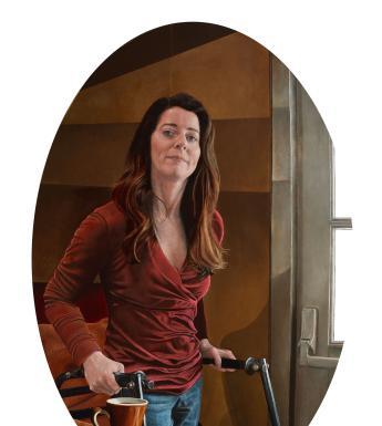 An oval-shaped portrait of a woman, wearing a red top and jeans and standing with the help of a walker. She looks directly at the viewer. On the table, a cup stands.