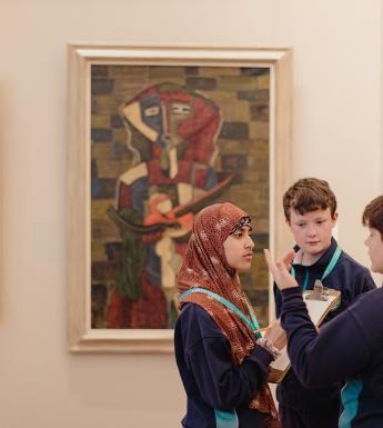 Three children stand together talking in front of three modernist paintings