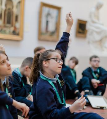 A group of young children in school uniform sit on the floor of an art gallery.