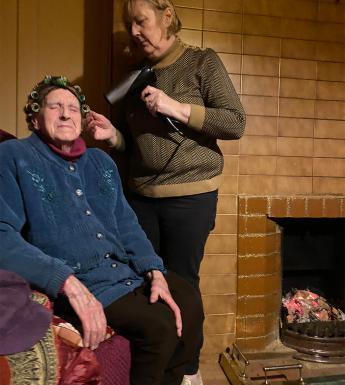 A photograph of a woman drying an older woman's hair in front of a fireplace