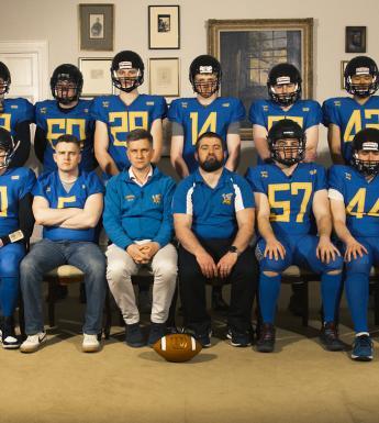 A photograph of an American football team, wearing their helmets and blue jerseys.