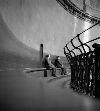 Black and white photograph of two men sitting on a bench within the curved dome of St Paul's Cathedral